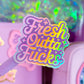 A close-up of a pastel pink pen with a holographic sticker that reads 'Fresh Outta' Fucks' in pink, purple, yellow, and blue gradient lettering. The background shows a matching lavender desk organizer with glittery compartments.
