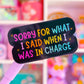 A close-up of a black novelty pen or stick with colorful text reading 'SORRY FOR WHAT I SAID WHEN I WAS IN CHARGE' in pink, yellow, blue, and white lettering, set against a blurred pastel toy or stationery shelf background.