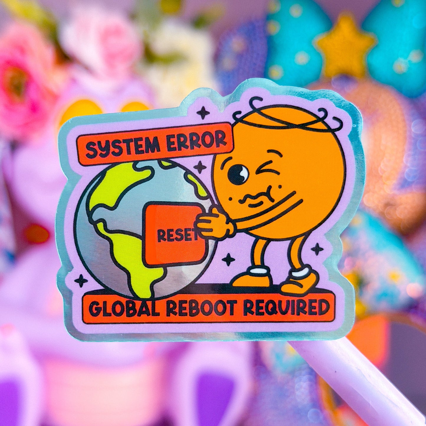 A colorful cartoon sticker or pin featuring an orange character winking while holding a globe, with text reading 'SYSTEM ERROR' and 'GLOBAL REBOOT REQUIRED', shown against a soft blurred pastel background.