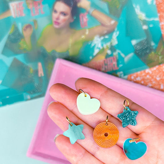 Hand holding colorful resin charms with a magazine and glittery material in the background