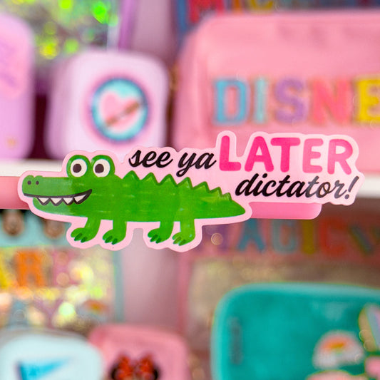 A close-up of a pink Disney-themed stationery organizer on a white shelf, featuring a green alligator sticker and a pink 'DISNEY' box in the background.
