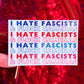 A hand holds a white sticker with the text 'I HATE FASCISTS & FLOCK CAMERAS' repeated in blue and red, set against a red sequined background.