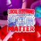 A die-cut sticker on a pink stick that reads 'LOCAL ELECTIONS democracy is calling! I VOTED MATTER' with cartoon ballot, box, and ballot-box characters. The sticker is photographed in a colorful, blurred setting with purple and red balloons in the background.