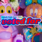 A colorful close-up of plush toys and decorative items with a large overlaid text graphic reading 'HAVE THE DAY YOU voted for'. The scene includes a lavender creature on the left, a glittery orange-and-blue character on the right, flowers at the top, and a mirror in the lower right.