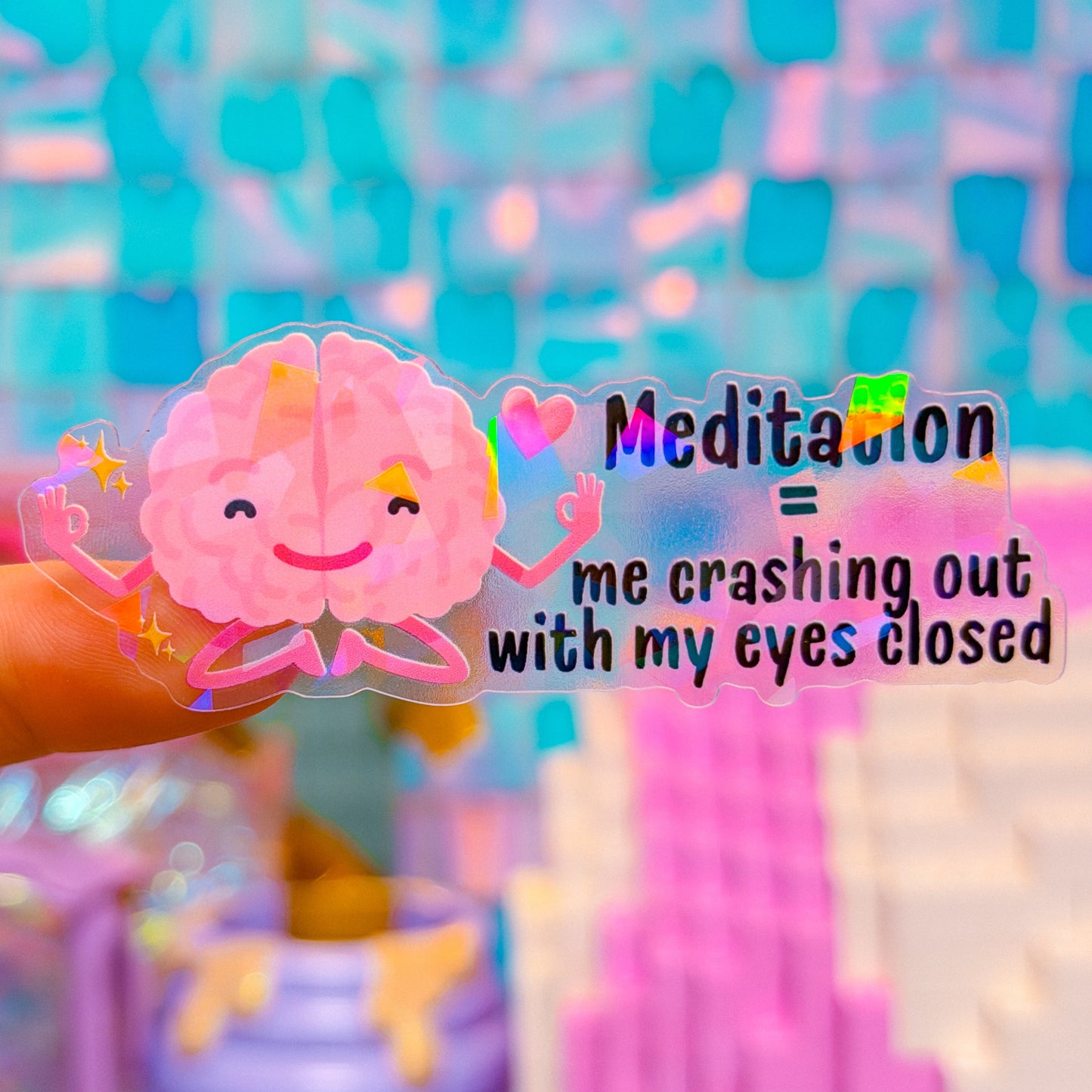 Pink cartoon brain sticker with text 'Meditation = me crashing out with my eyes closed' on a colorful blurred background.